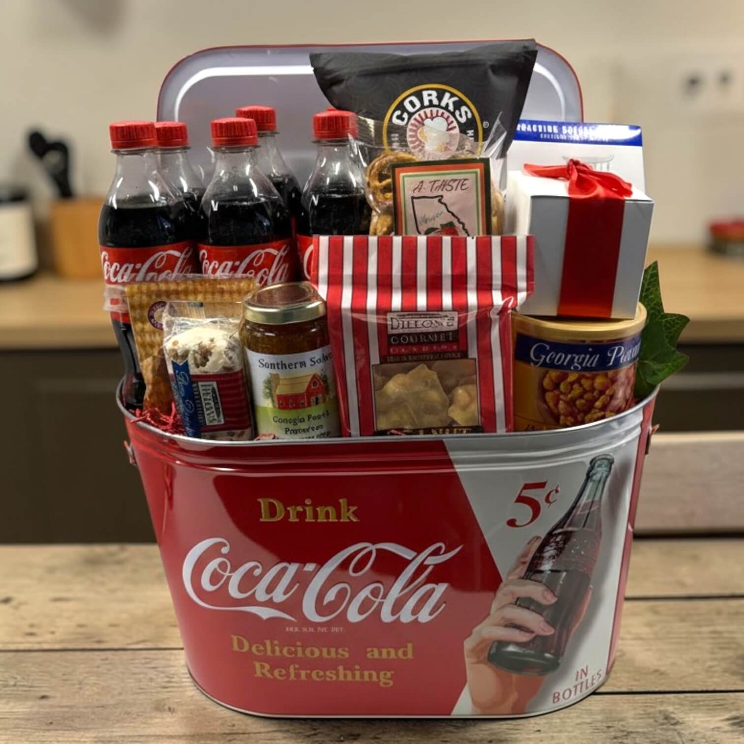 Coca-Cola gift basket with snacks and drinks in a metal party tub sitting on a wooden surface