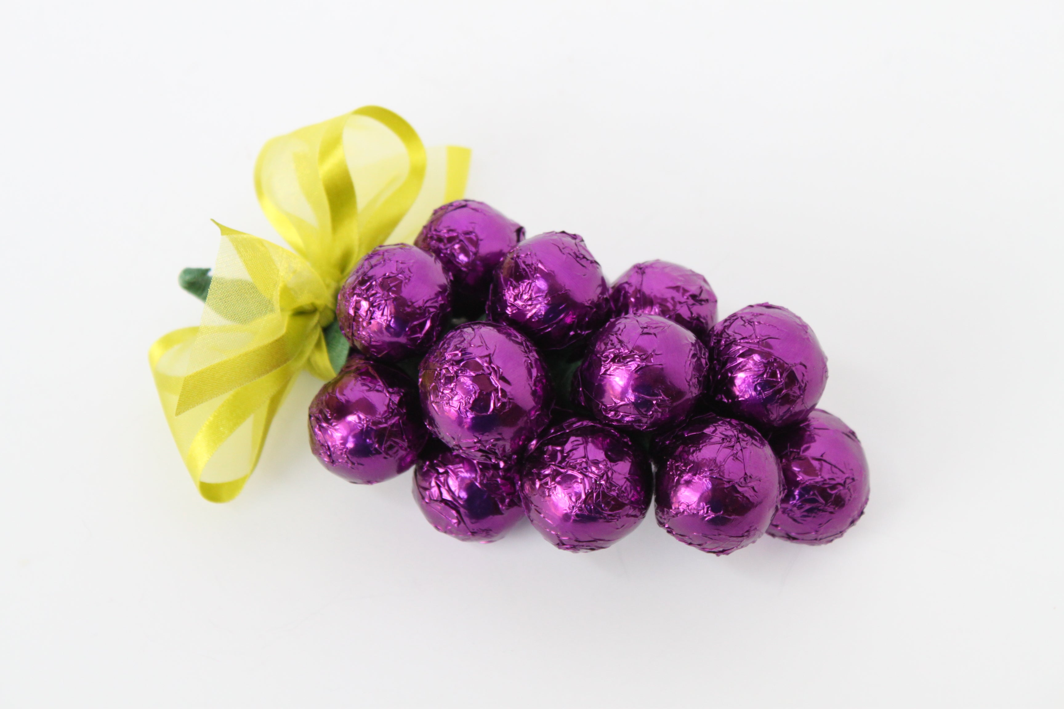 Purple foil wrapped chocolate grape cluster with a yellow ribbon on a white background