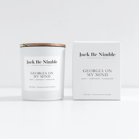 A peach scented soy candle jar with a light wood lid sits beside its white product box. The labels read Georgia On My Mind, with small scent notes peach, watermelon, and honeysuckle.