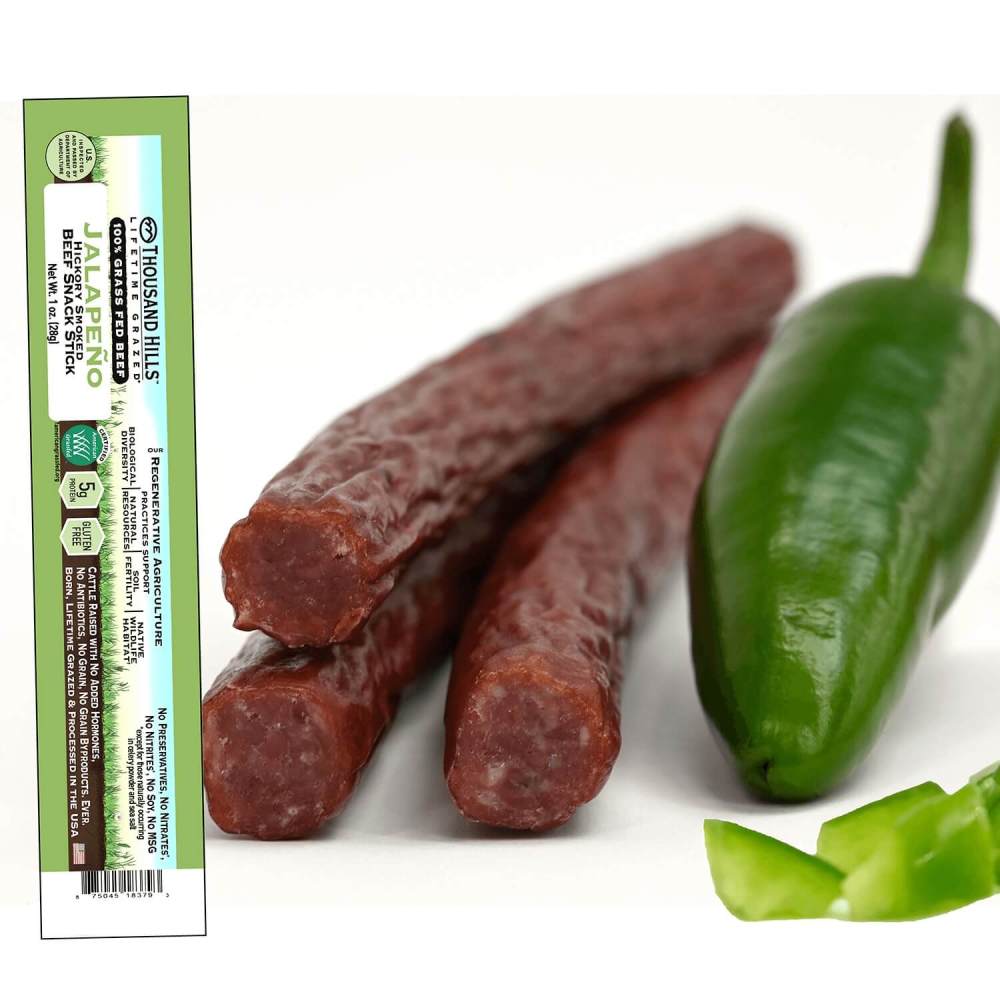Two dried jalapeno pepper beef sticks with a green label on the left and a fresh jalapeno pepper on the right.