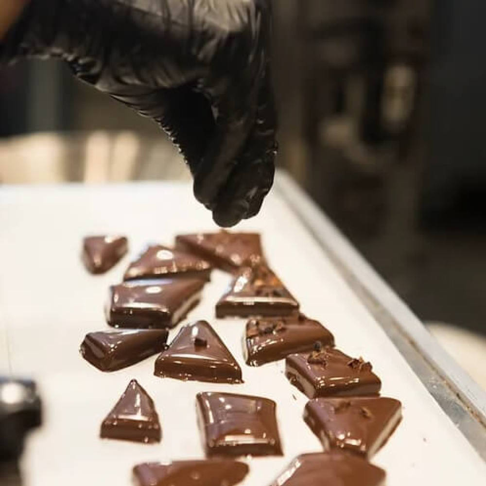 Chocolate English toffee pieces on a tray with a gloved hand reaching towards them