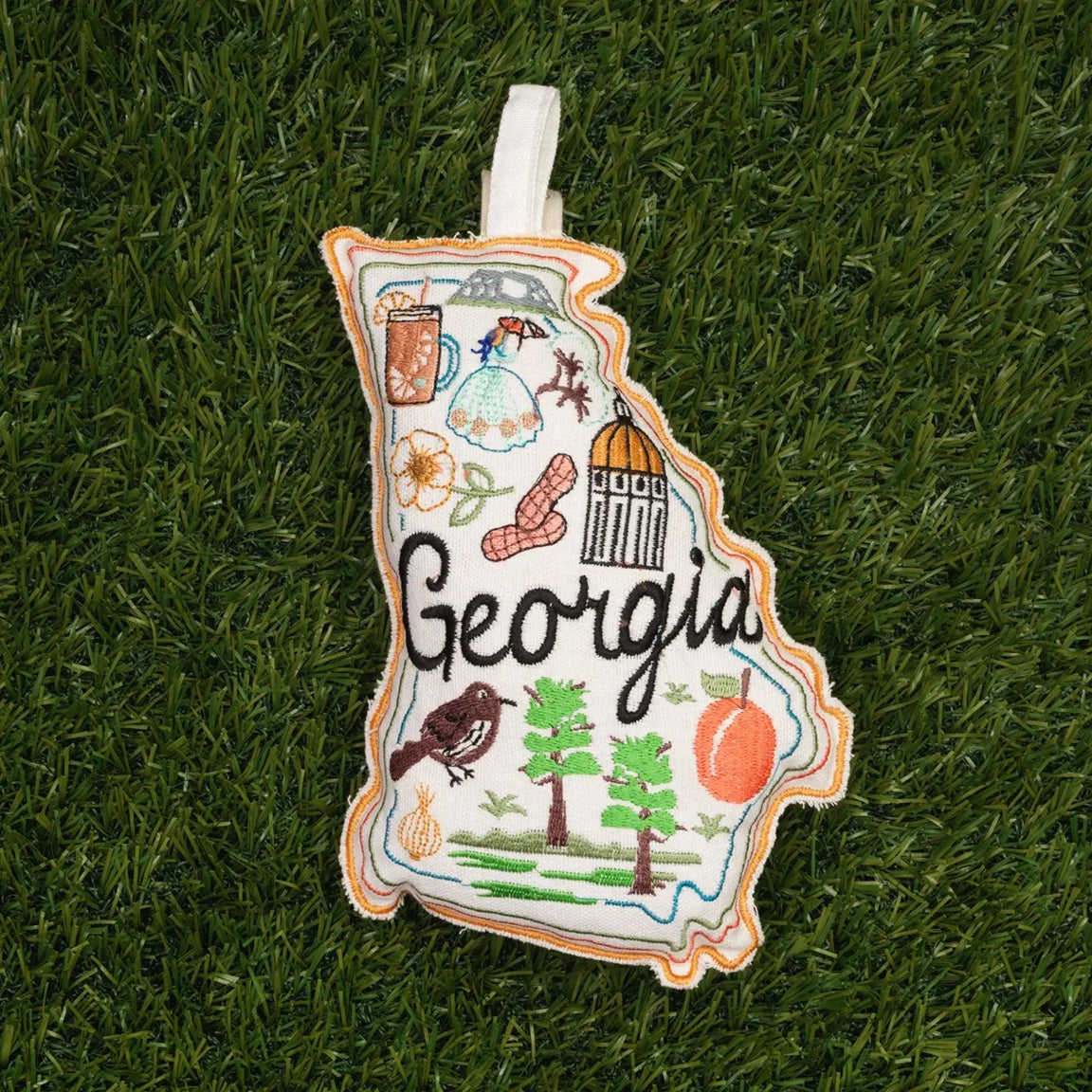 Embroidered pet toy of the state of Georgia on a grass background