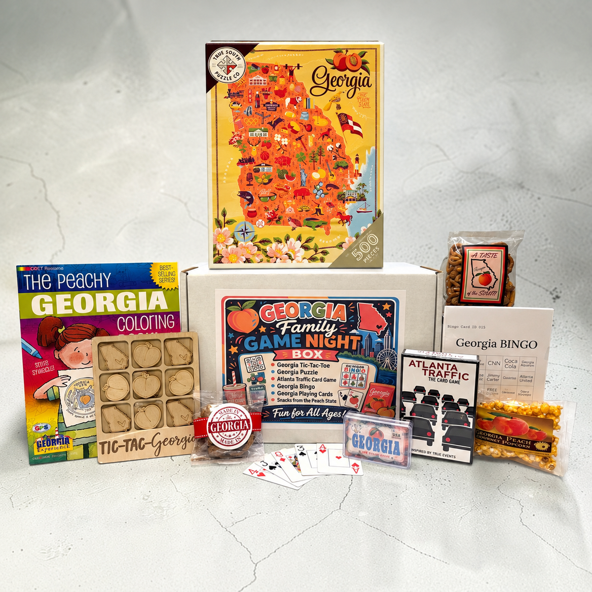 Group picture of a Georgia game night theme gift box with coloring book, tic-tac-toe, Atlanta Traffic card game, Georgia puzzle, Georgia Bingo, playing cards and snacks from Georgia.