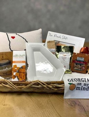Gift basket with various Georgia theme items including a pillow, cheese straws, and a Georgia towel on a wooden surface.