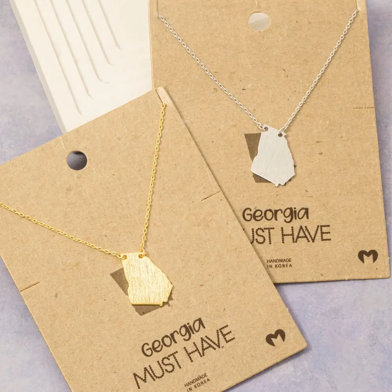 Two Georgia shaped necklaces on brown cards with &