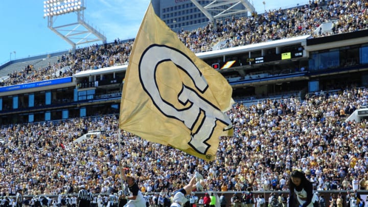 Large crowd in a stadium with a person holding a yellow flag featuring 'GT' in the foreground.