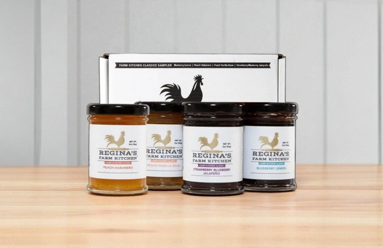 Three jars of Regina's Farm Kitchen jam on a wooden surface with a box in the background.