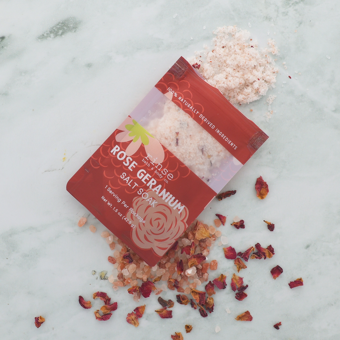 Rose Geranium salt soak packaging with scattered rose petals on a marble surface