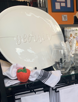 White plate with 'georgia' text on a kitchen counter with a glass and small decorative items.