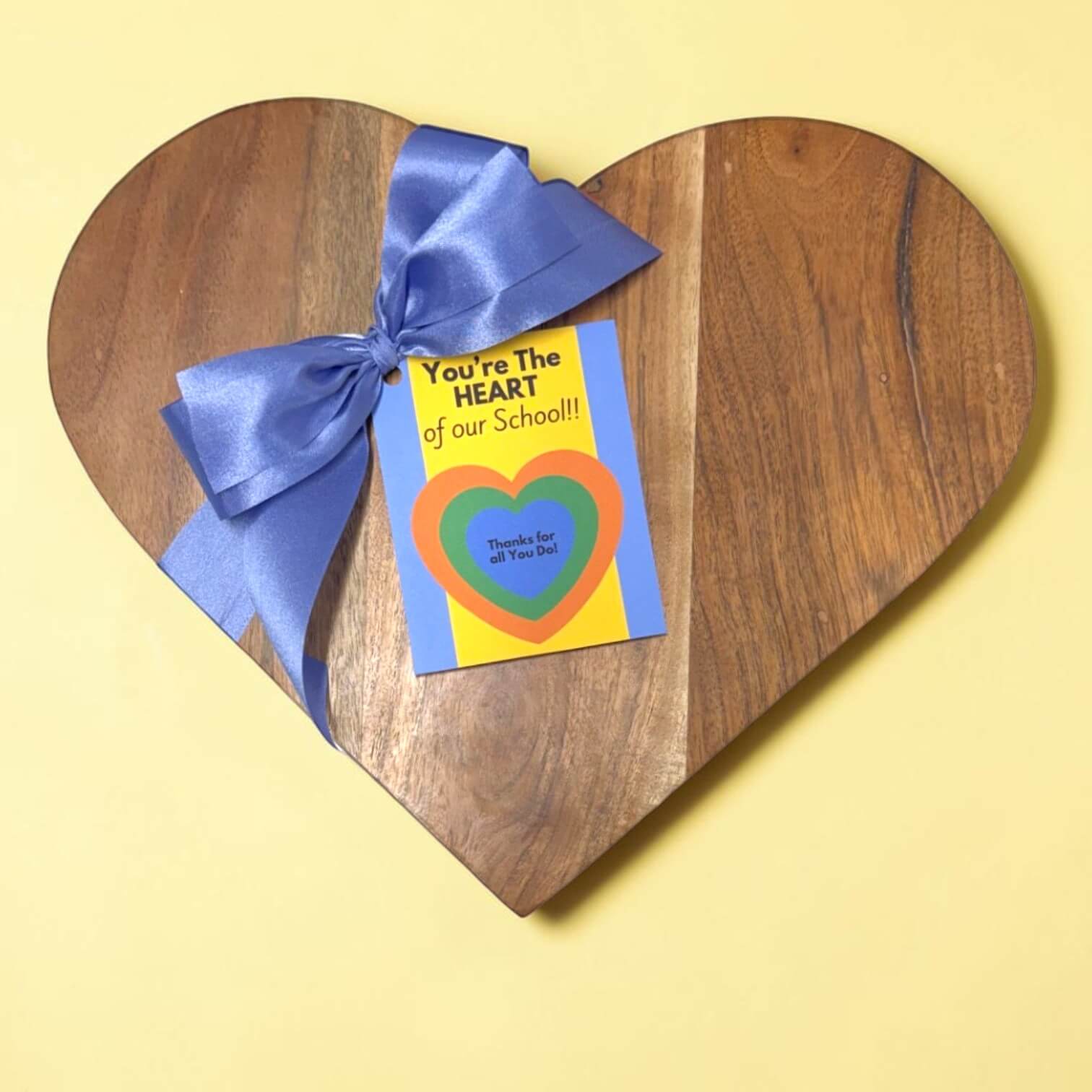 Heart-shaped wooden board with a blue ribbon and a card on a yellow background