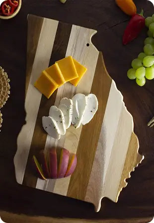 Wooden cutting board in the shape of Georgia with cheese and fruits on a dark surface