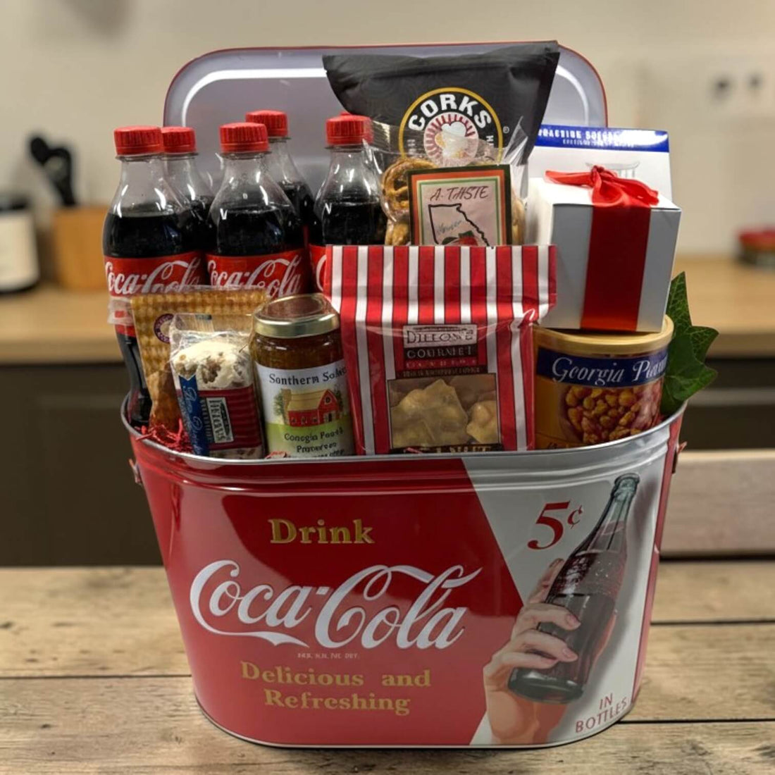 Coca-Cola gift basket with snacks and drinks in a metal party tub sitting on a wooden surface
