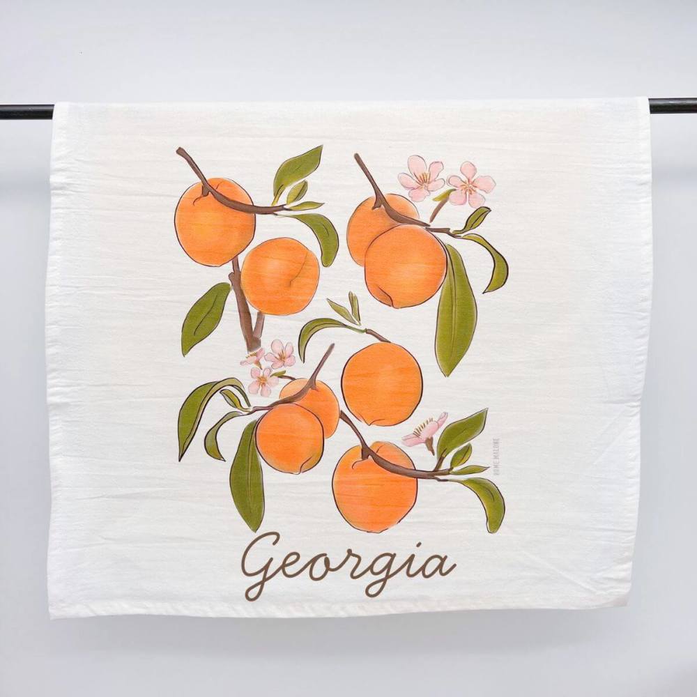 White flour sack kitchen towel with lovely peaches in a cascading design and the Georgia state name.