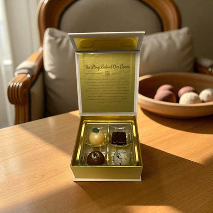 Gold box with four artisan chocolates on a wooden table with a distinctive chair in the background