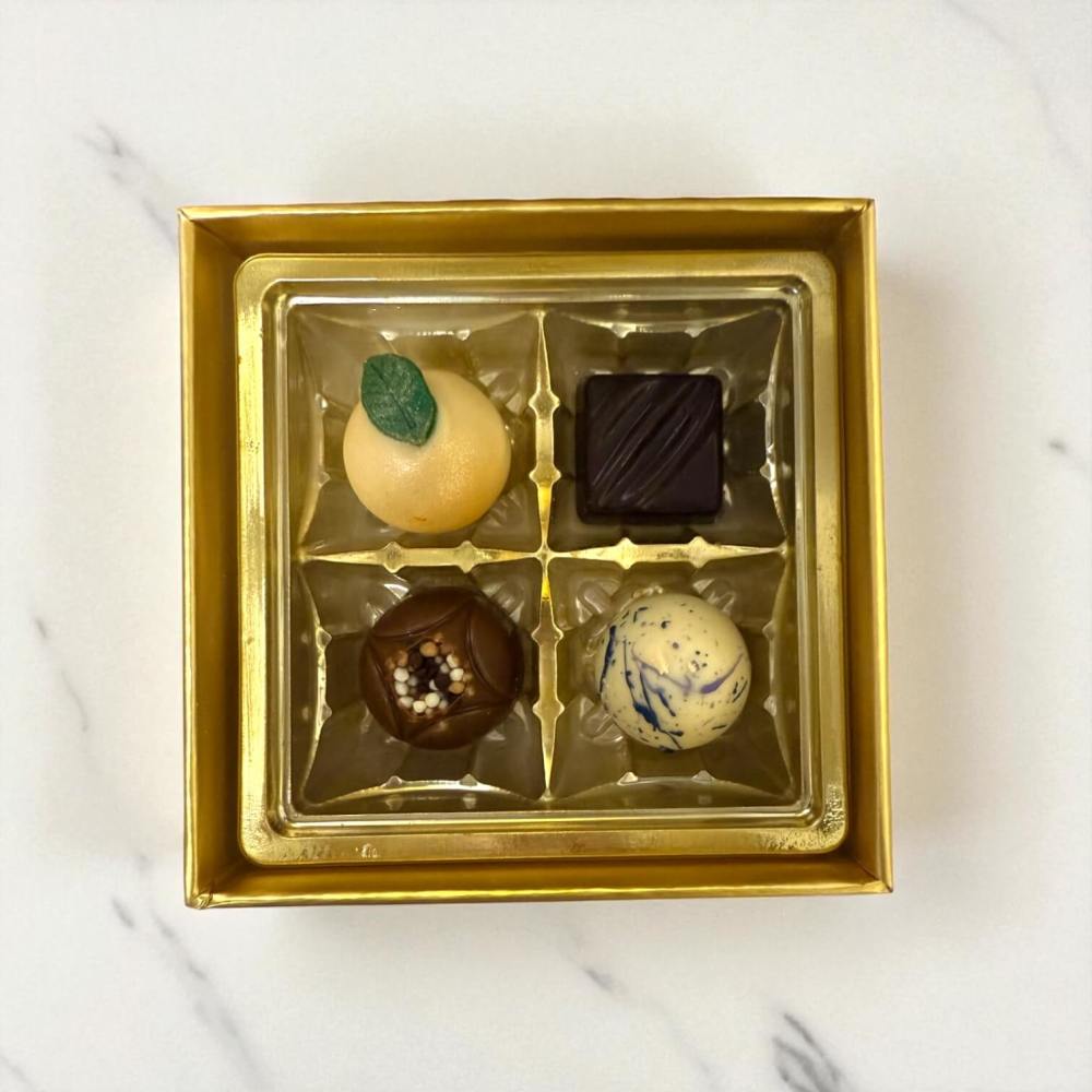 Gold box with four assorted artisan chocolates on a marble surface