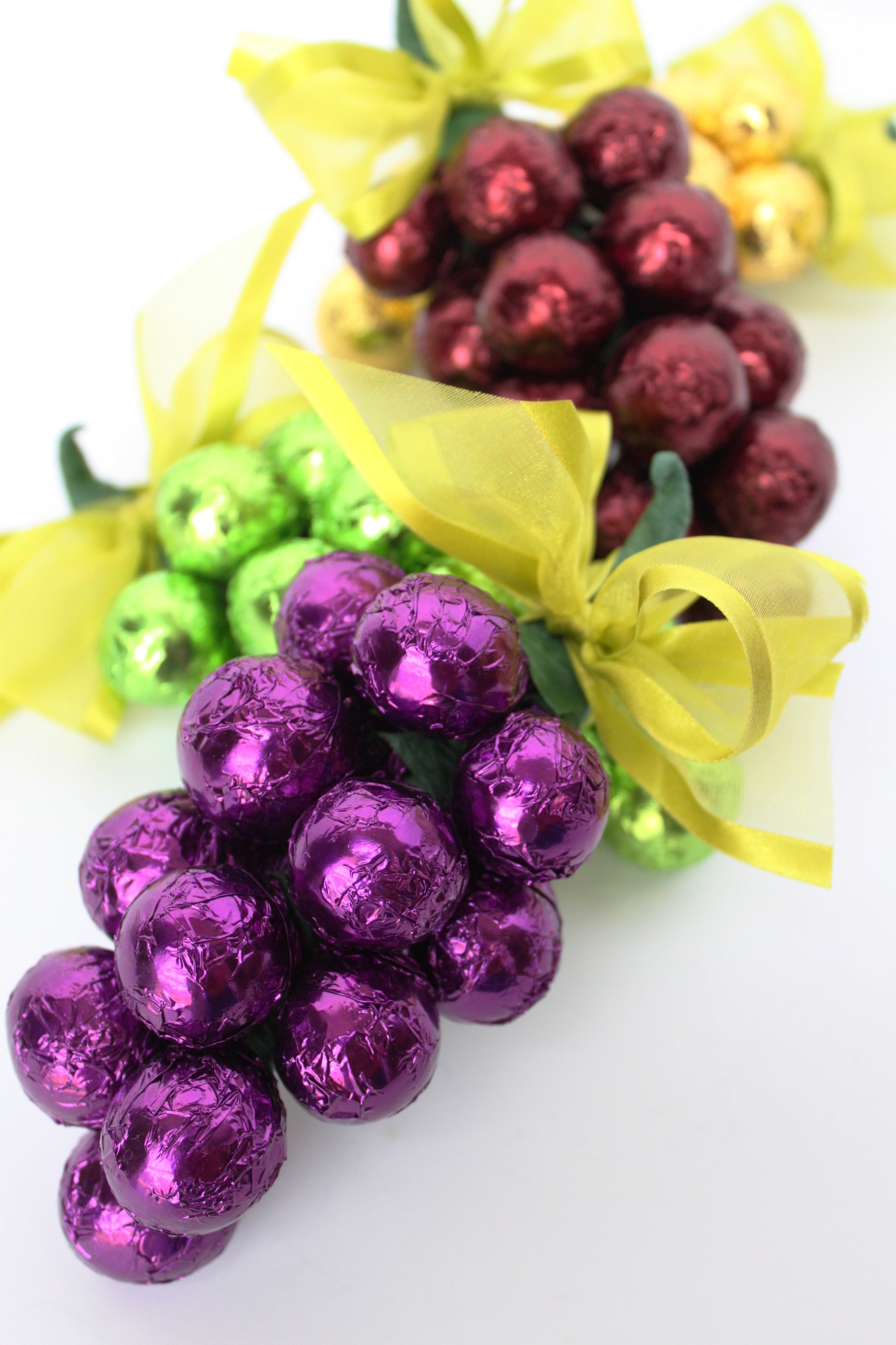 Decorative chocolate grapes in purple, green, and red with yellow ribbons on a white background