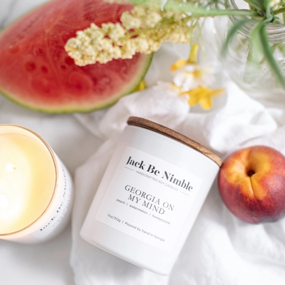 Peach scented Georgia On My Mind Candle with a watermelon, peach, and flowers on a white surface