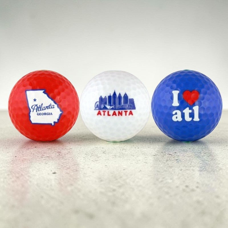 three Atlanta theme golf balls in red, white and blue with Atlanta skyline, state and I love ATL designs on marble table.