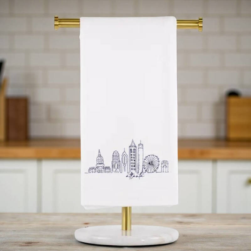 White towel with Atlanta city skyline design on a gold towel rack against a kitchen background