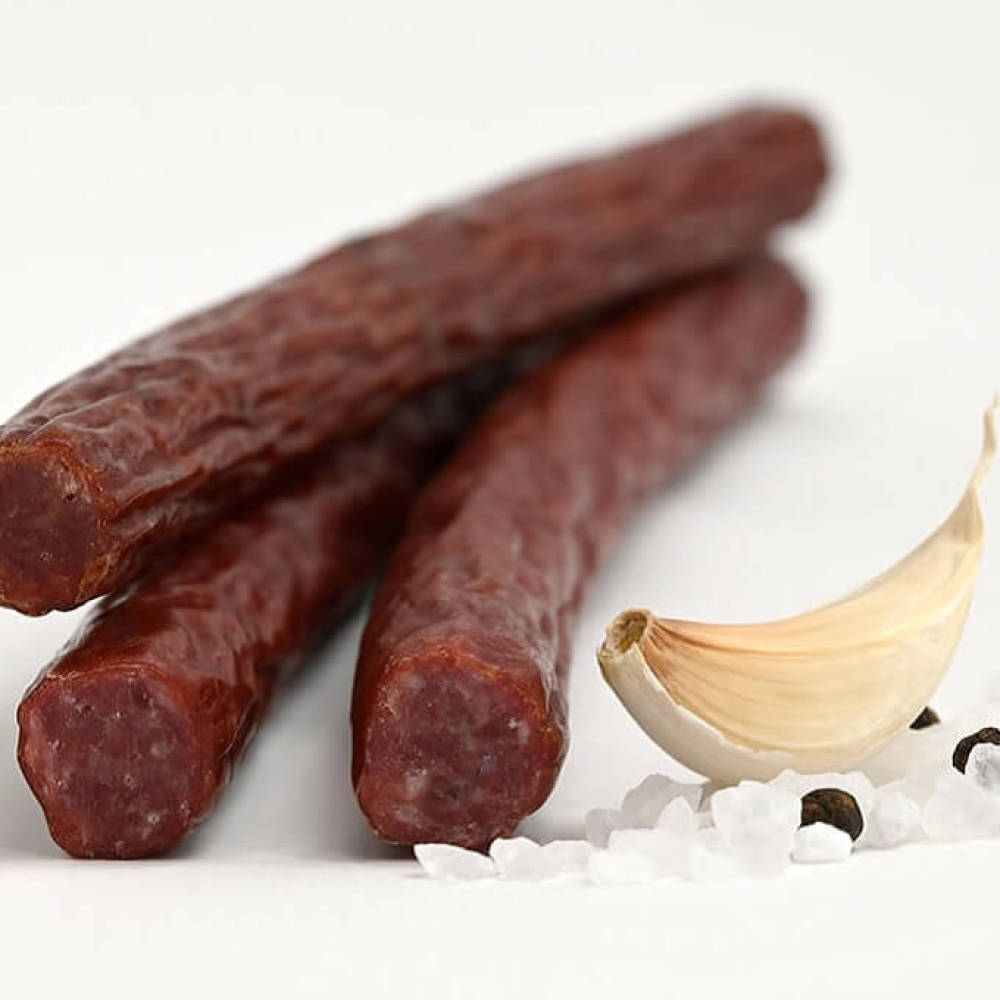 Group of four snack beef sticks next to garlic clove and seasonings