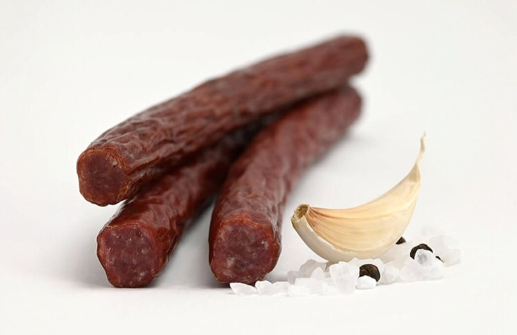 Three beef sticks with garlic and salt on a white background
