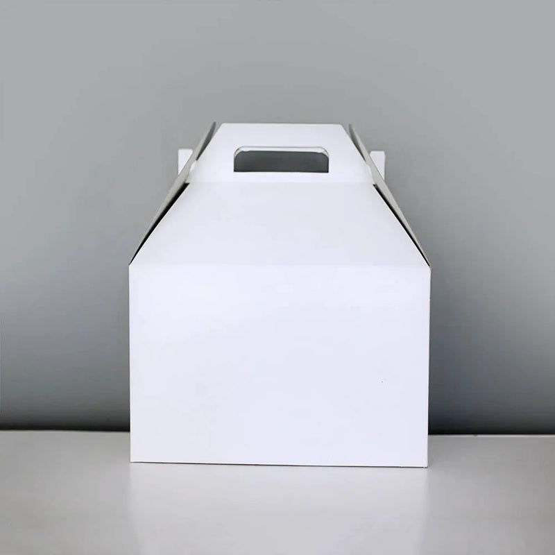 A plain white rectangular cardboard gable box with a top handle cutout, standing upright on a light surface against a gray background.