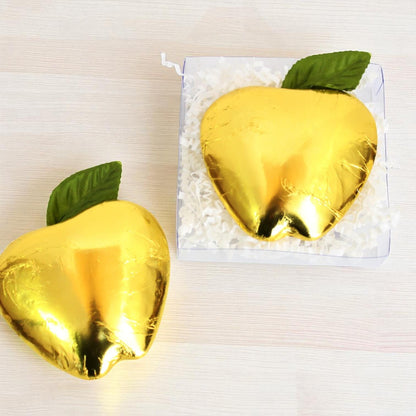 Gold foil-wrapped chocolate apples with green leaves on a white background
