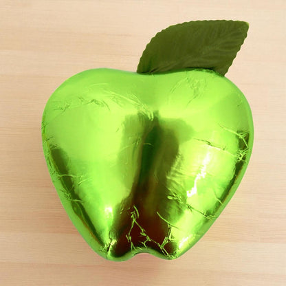 Green foil-wrapped chocolate shaped like an apple on a beige background