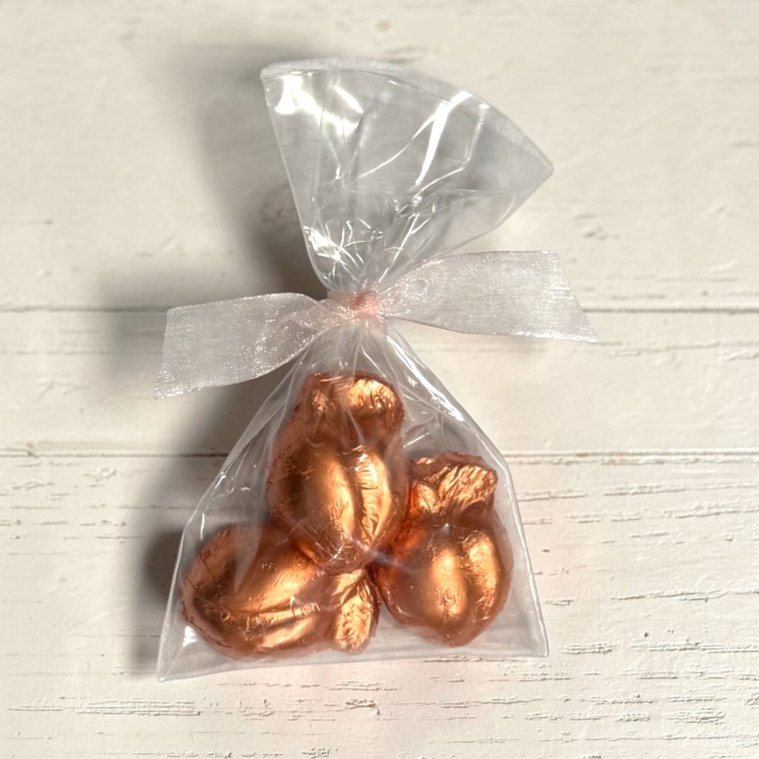 Three peach-shaped chocolates wrapped in copper foil in a clear cellophane bag on a light wooden surface