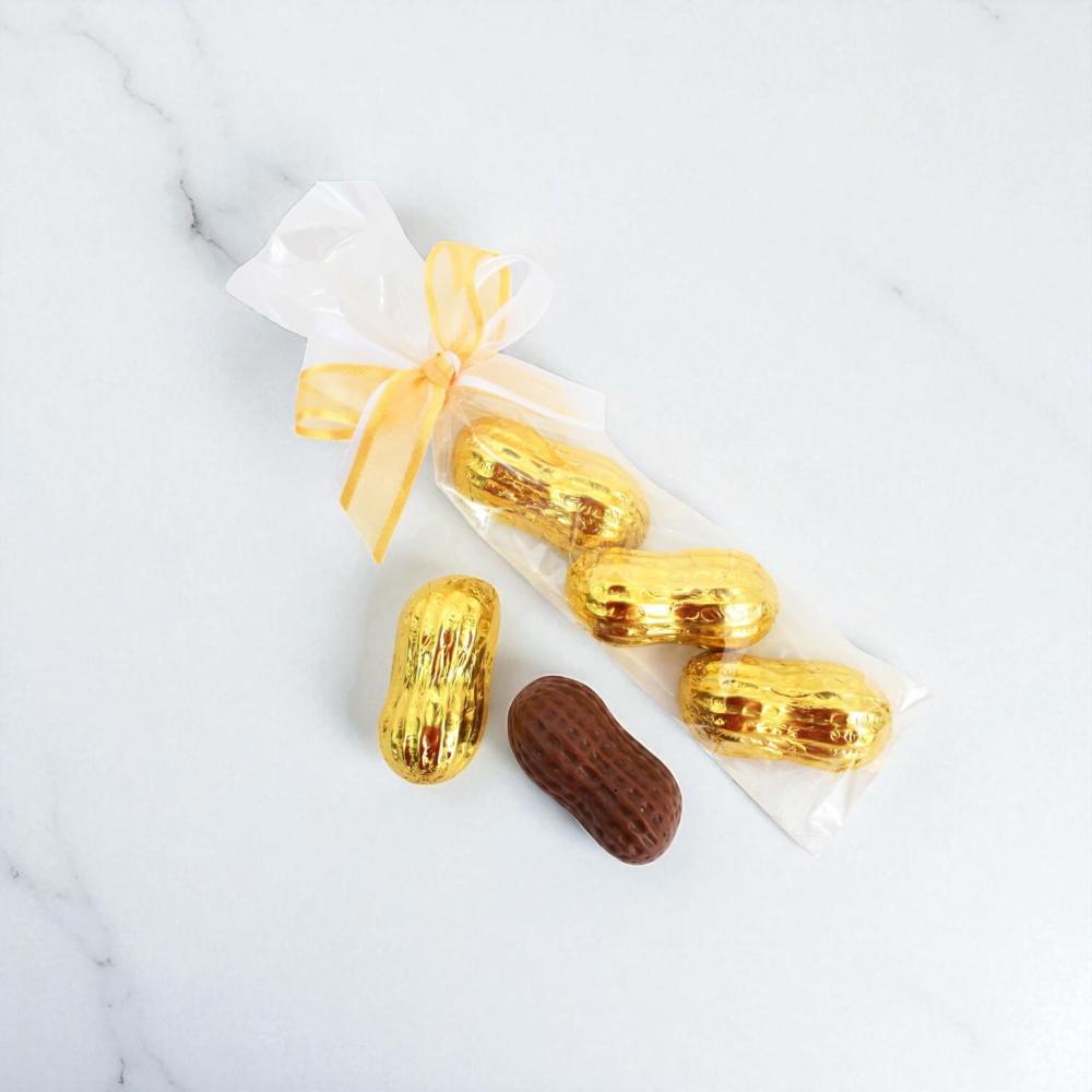 Gold-wrapped peanut shaped chocolate candies with an unwrapped chocolate peanut on a white background