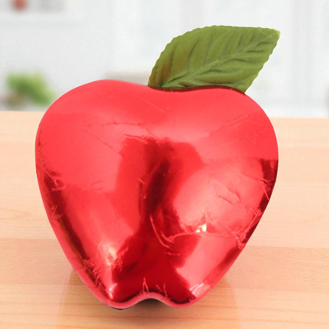 Red apple-shaped chocolate with a green leaf on a wooden surface