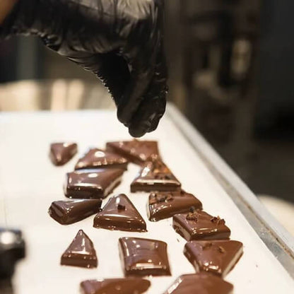 Chocolate English toffee pieces on a tray with a gloved hand reaching towards them
