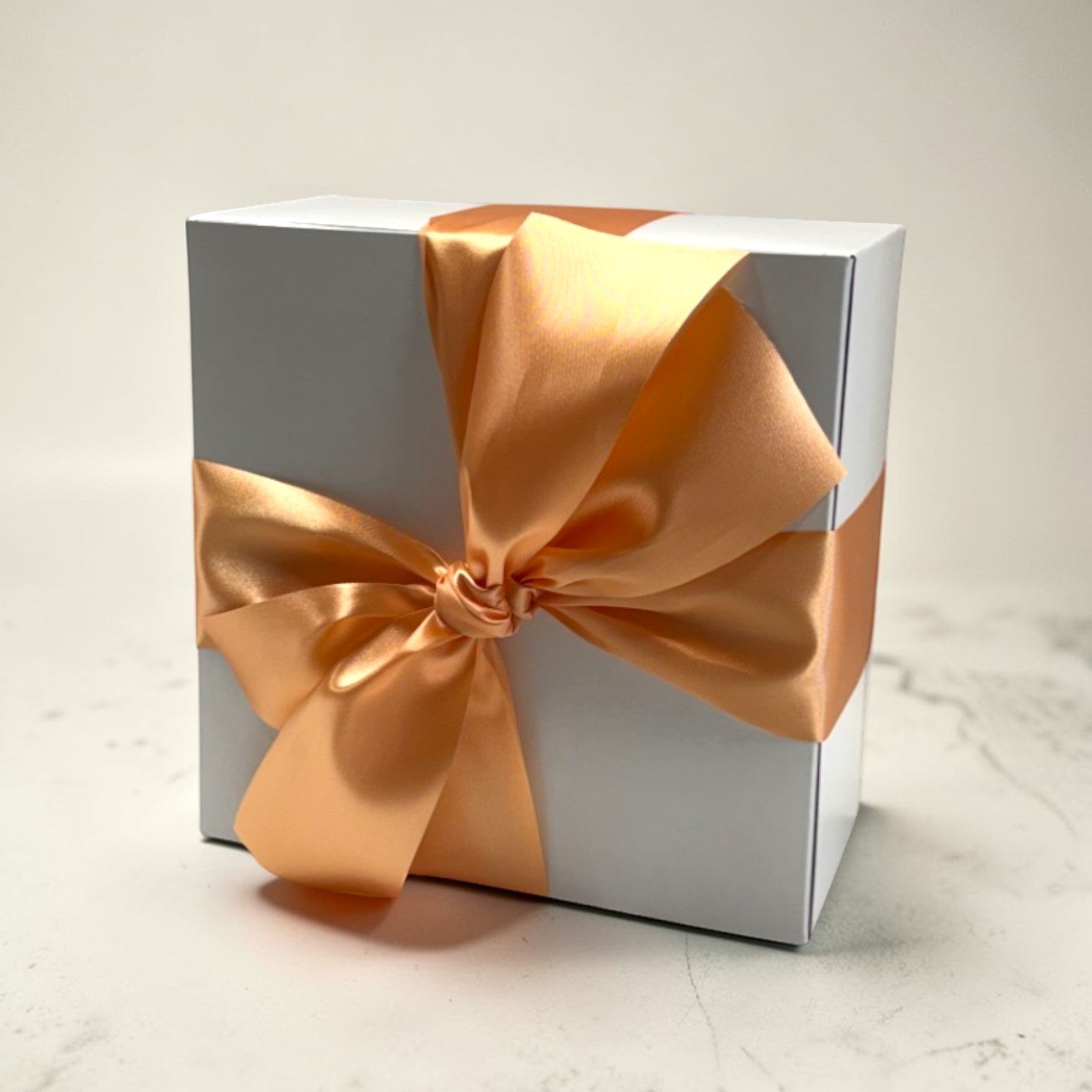 White gift box with a large peach color bow on a light background