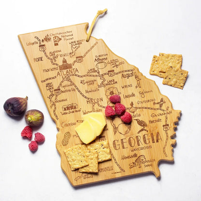 Wooden cutting board shaped like the state of Georgia with engraved details, surrounded by food items on a white background.