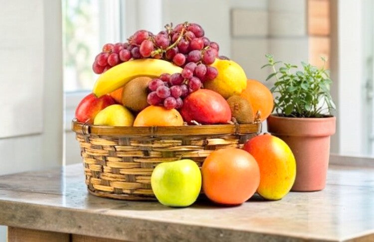 Basket of fruits including grapes, apples, and oranges in a wicker bowl on a marble table.