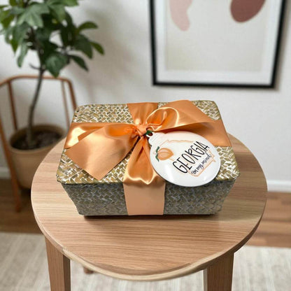 Rattan chest with a peach ribbon and Georgia ornament on a wooden table, indoor setting