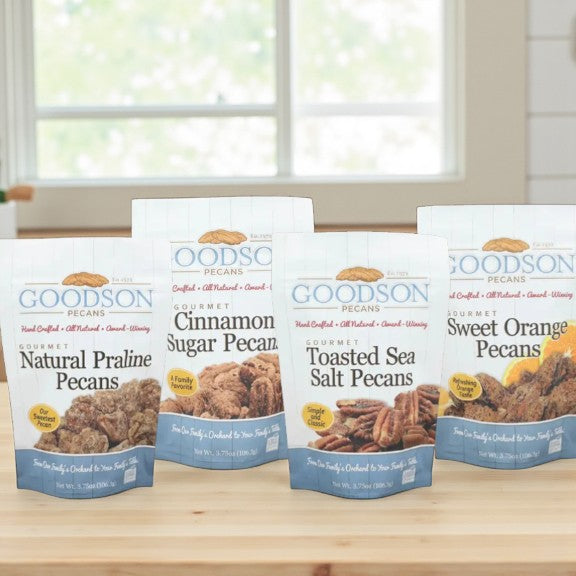 Four packages of Goodson Pecans on a wooden surface with a window in the background.