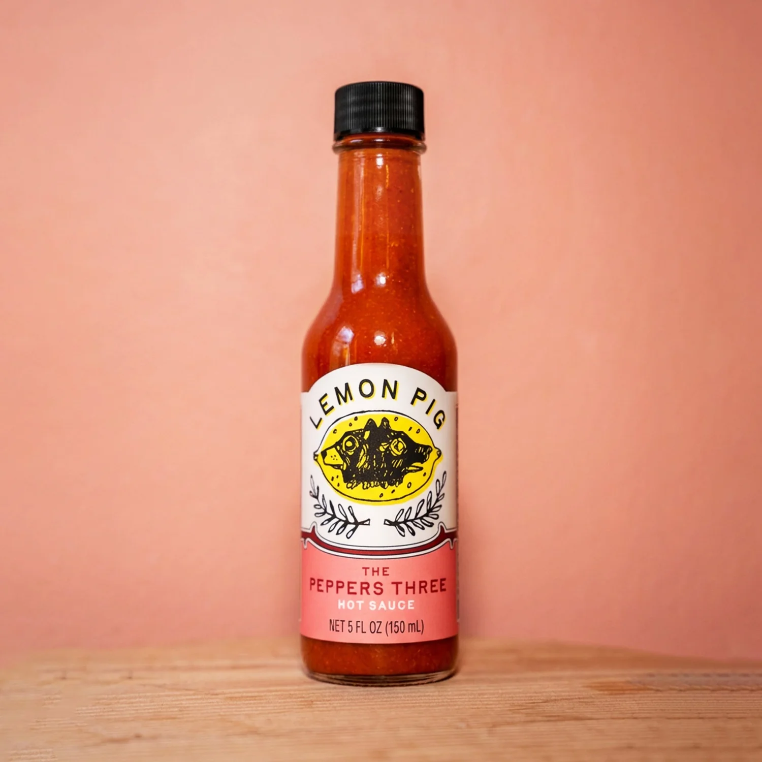 Hot sauce bottle with Lemon Pig label on a pink background