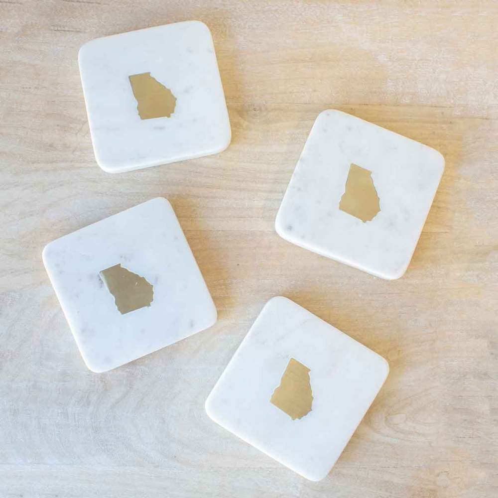 Set of four white marble coasters with the state of Georgia shape made of brass in the center.