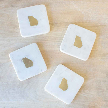 Set of four white marble coasters with the state of Georgia shape made of brass in the center.