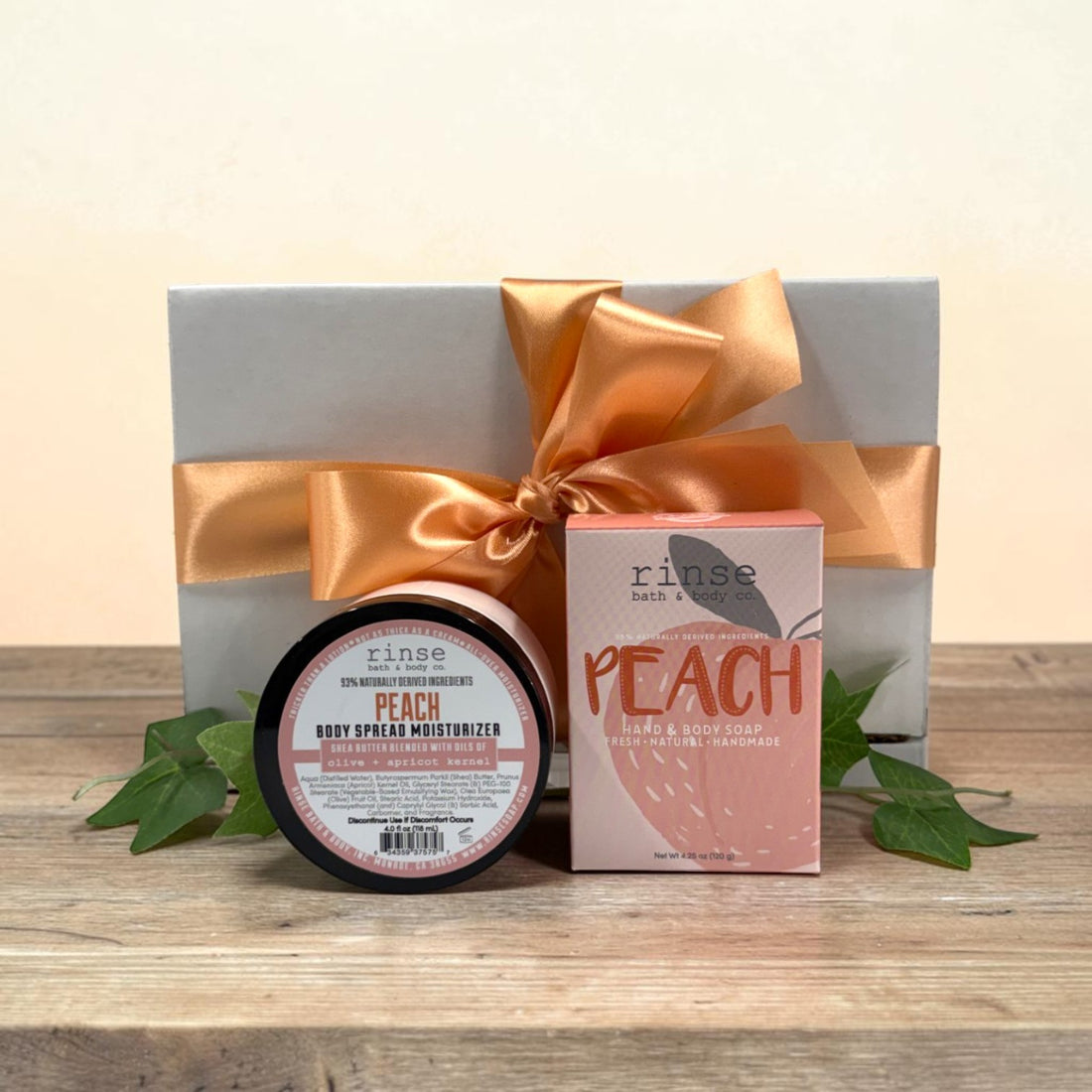 Gift set with Peach soap and body spread moisturizer in front of a white gift box on a wooden surface.