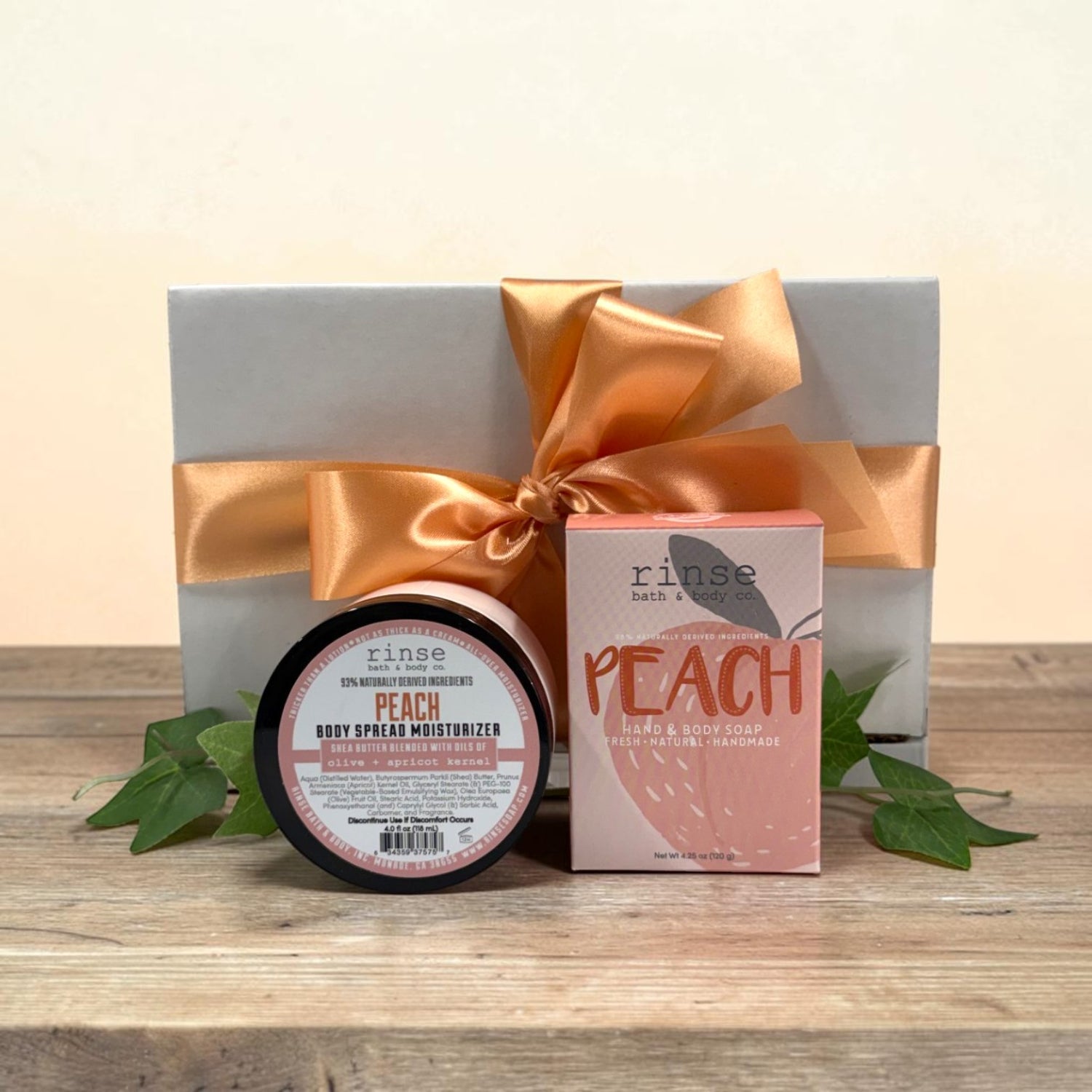 Gift set with Peach soap and body spread moisturizer in front of a white gift box on a wooden surface.