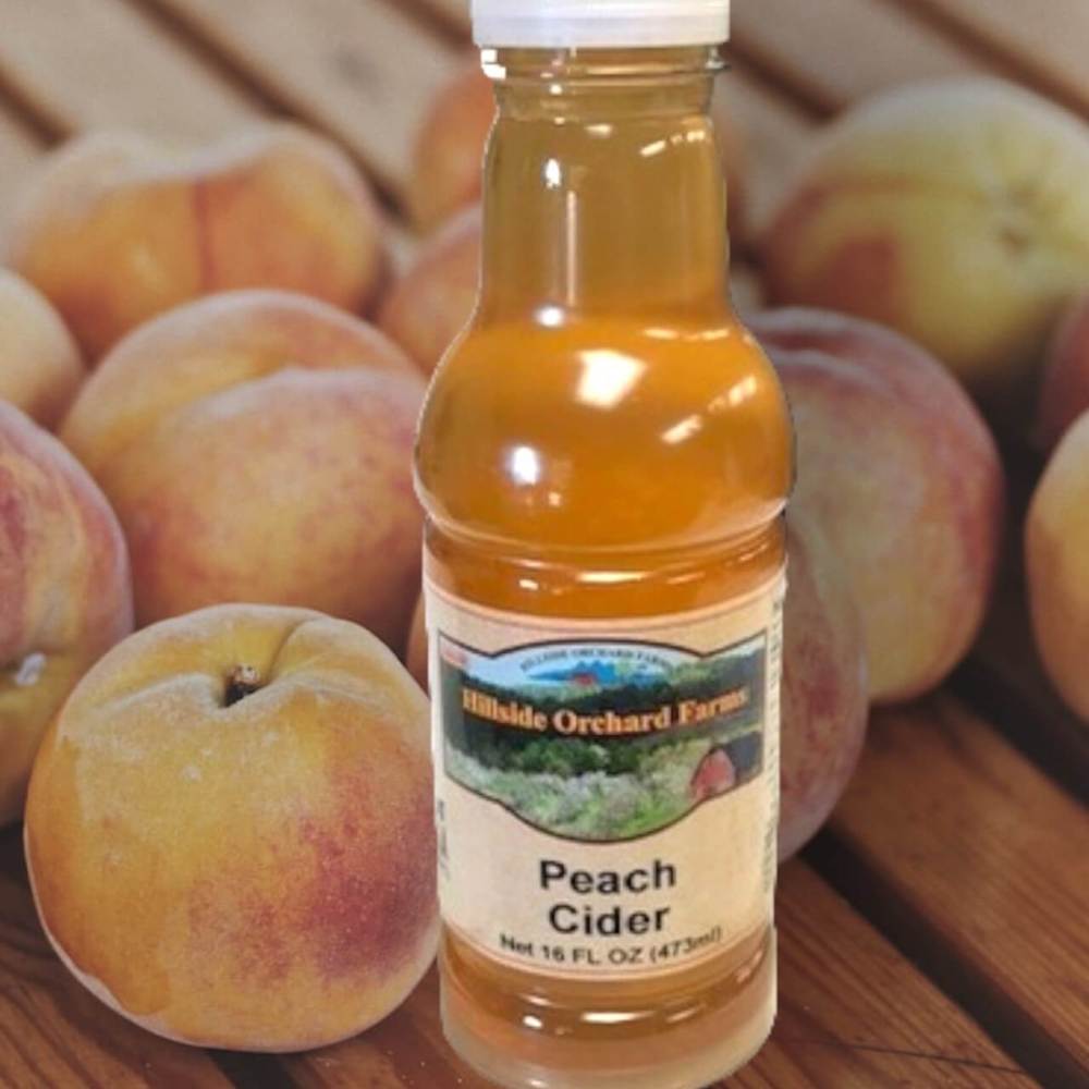 Georgia Peach Cider in 16 oz. bottle surrounded by fresh Georgia peaches.