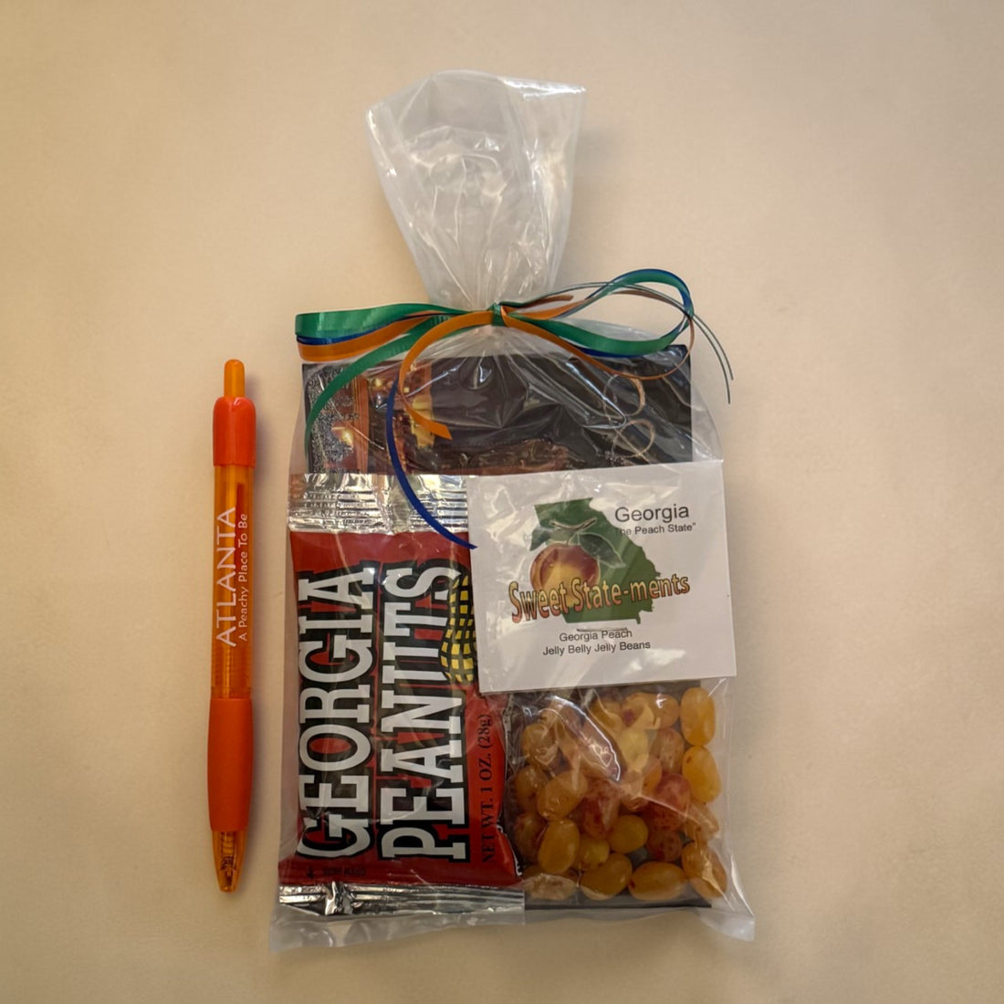 Packaged snacks and souvenirs from Georgia including peanuts, jelly beans, postcard and a pen on a beige background