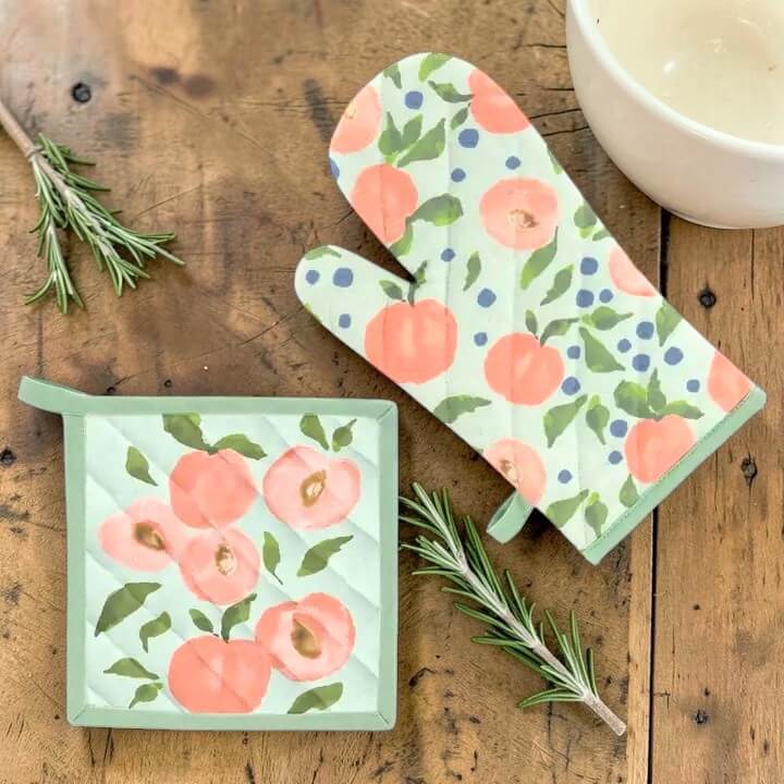 peach-patterned pot holder and mitt on a wooden surface with rosemary sprigs.
