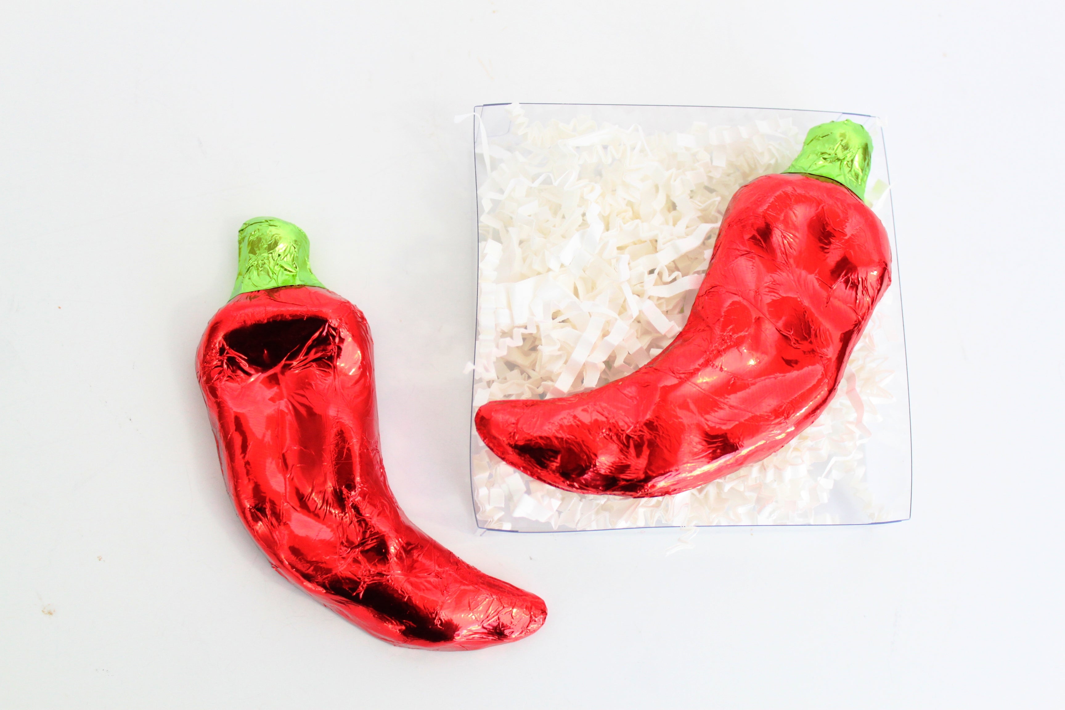 Red chili pepper-shaped chocolates wrapped in foil on a white background