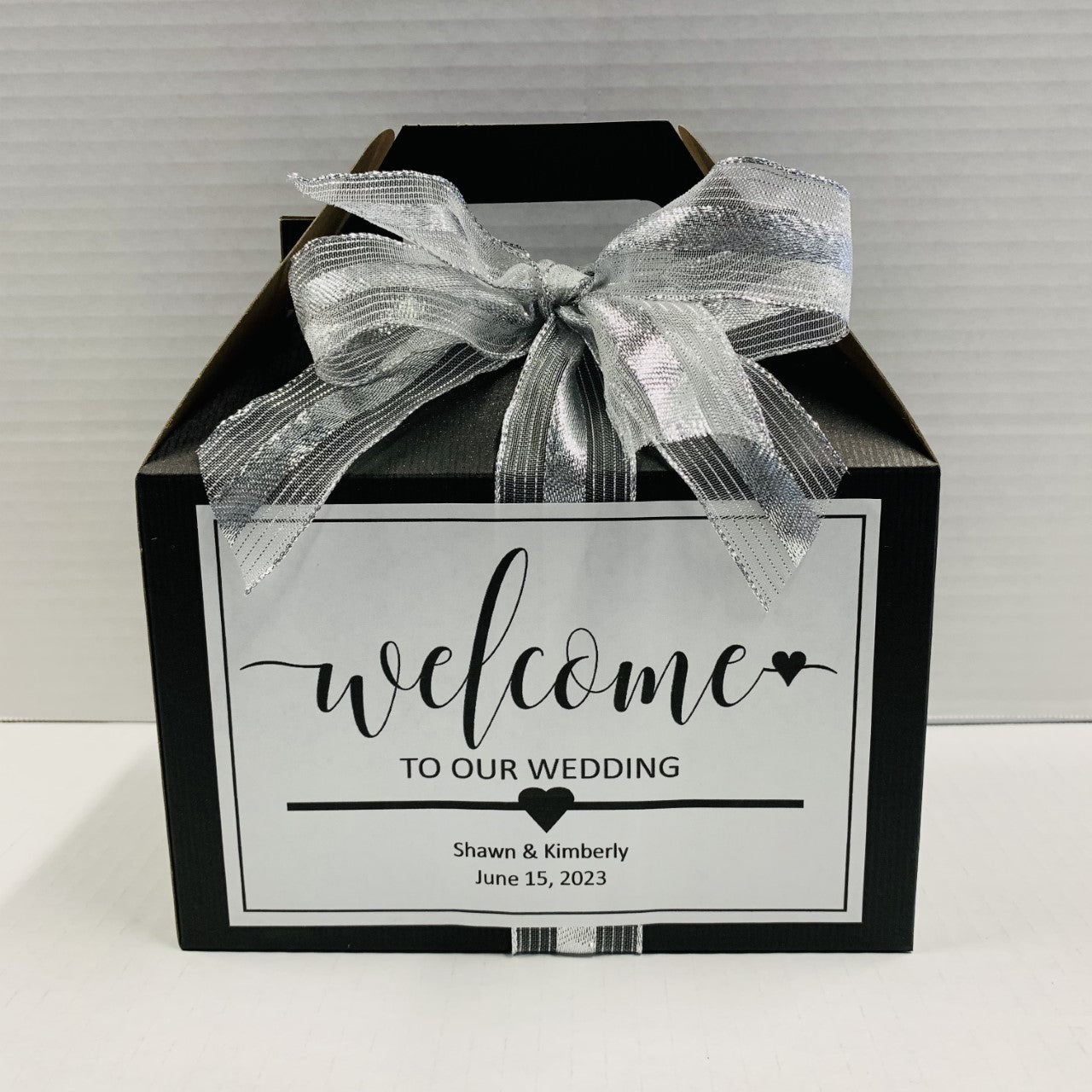 Black gift box with a silver ribbon and personalized wedding welcome label.