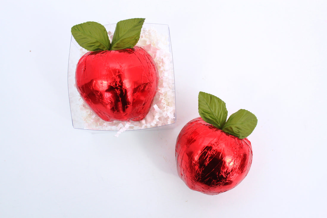 Two red chocolate apples with green leaves on a white background