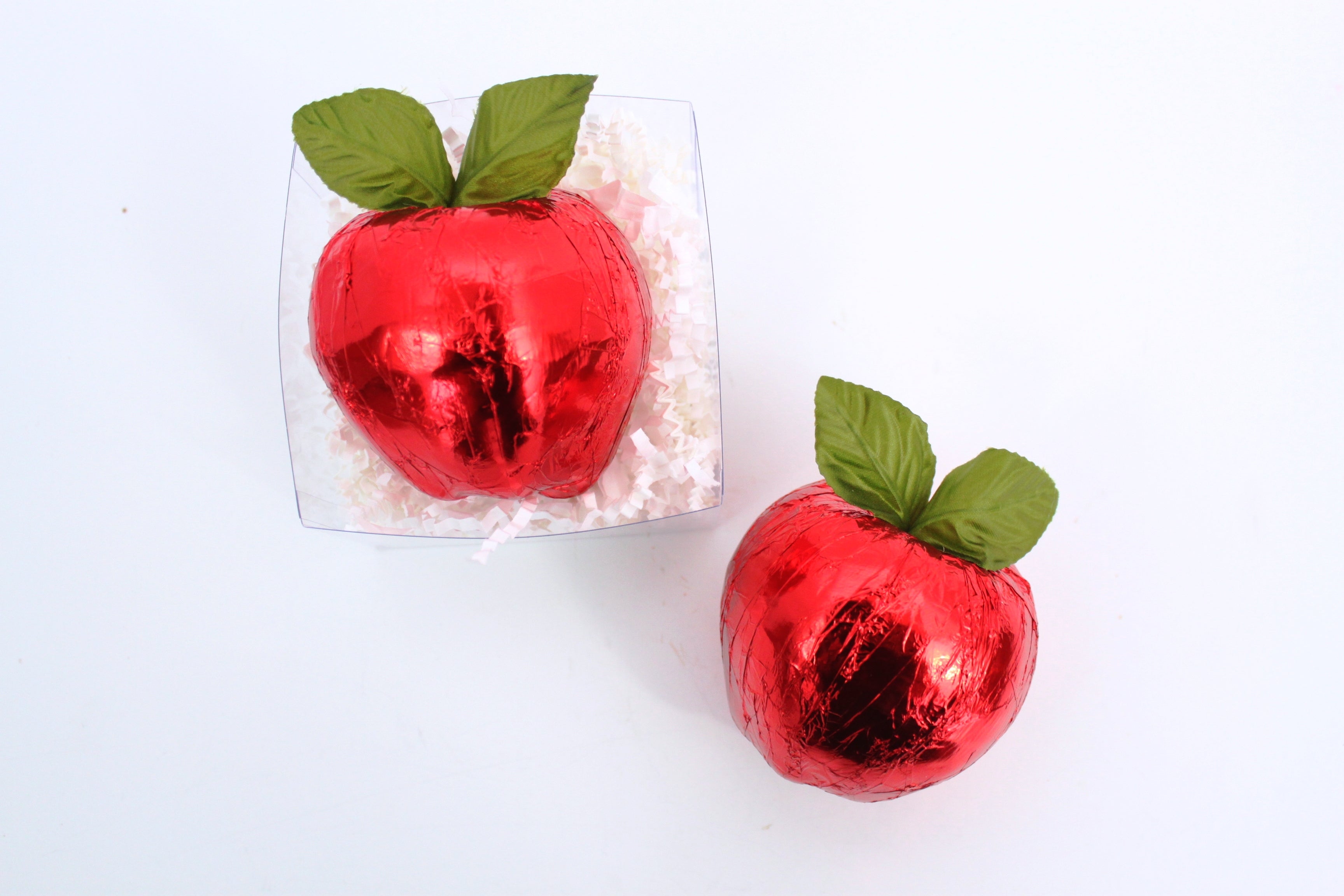 Two red chocolate apples with green leaves on a white background