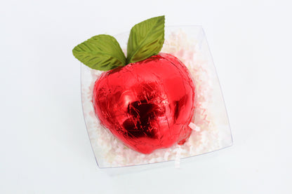 Red foil-wrapped chocolate in the shape of an apple with green leaves on a white background